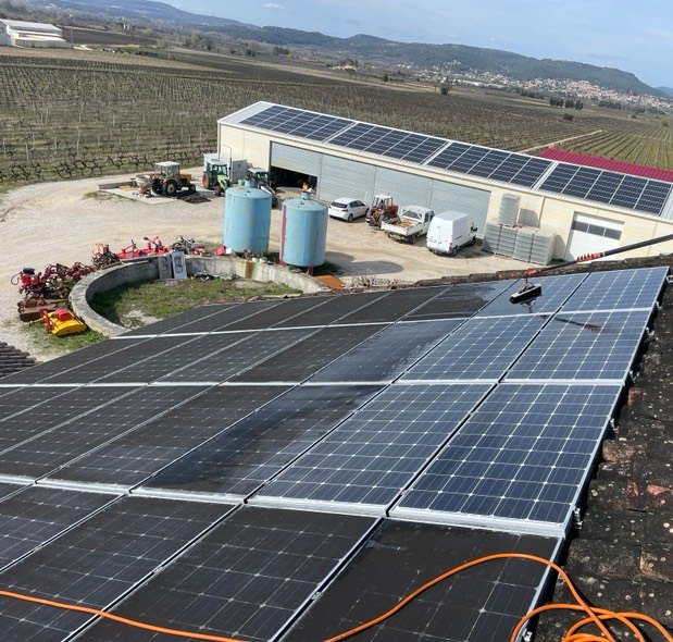 Panneaux photovoltaïques en cours de lavage sur une centrale en Vaucluse, hangar agricole en arrière-plan